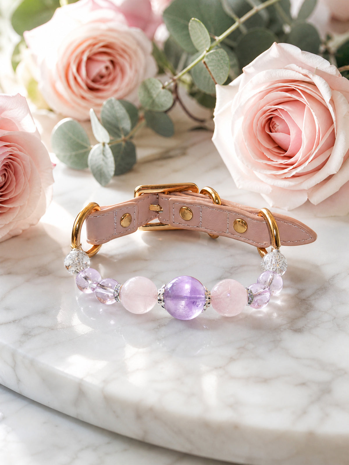 SoulBond Crystal Charm Pet Collar with pink and purple beads displayed beside pink roses on a white veined surface